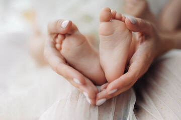 Obraz na płótnie Canvas Baby feet in mother hands. Tiny Newborn Baby's feet on female Shaped hands closeup. Mom and her Child. Happy Family concept. Beautiful conceptual image of Maternity