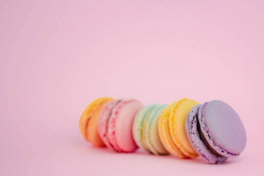 Low angle close up view of an assortment of colorful French macarons on pink background with selective focus