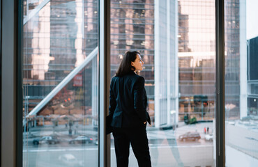 Young businesswoman standing against big window with hand in pocket