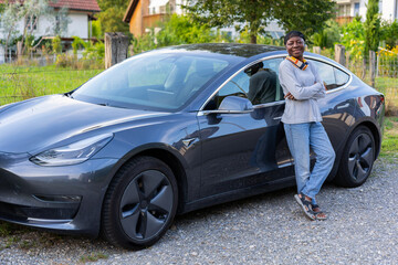 Side view of happy African woman standing in front of her car.