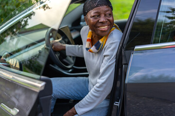 Side view of African woman sitting in electric car with open door smiles backward.