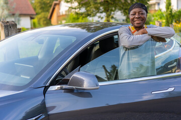 Electric car with happy African woman standing in open car door.