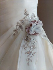 Close-up of embroidery in flower pattern on a wedding dress. Textile in different tones in beige and white against beige background. 