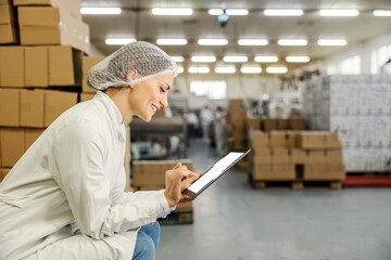 A food factory manager is crouching and scrolling on tablet in facility.