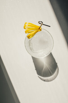 Directly Above, Soda Water With Ice And Cut Lemon Peel Garnish On Cocktail Pick In The Sun