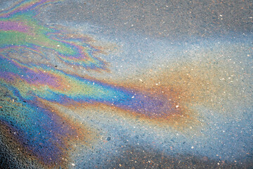 Close-up of an iridescent oil or gasoline spill on a wet asphalt, viewed from above. Bold...