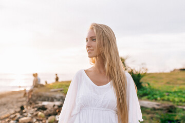 Fototapeta na wymiar Elegant woman with long hair wearing white shirt with happy smile looking aside and enjoying ocean view in sunny warm day. Relax, vacation mood
