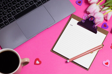 Female workspace with laptop, tulips, accessories, notebook, cup of coffee on pink background