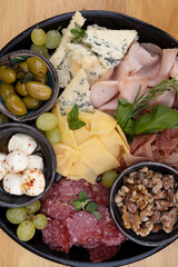 Cold cuts. Top view of a dish with sliced salami, cheese, blue cheese, italian boconccinos, walnuts, ham, cured ham and green olives, on the wooden table.