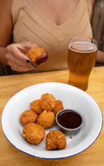 Eating fried chicken croquettes with a spicy sauce and a pint of beer.