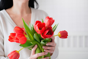 International Womens Day.Close-up of a woman in a white sweater with a bouquet of red tulips