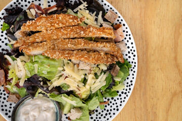 Caesar salad. Closeup view of fresh a salad with lettuce, parmesan cheese, bread croutons, sliced grilled chicken breast, bacon and Caesar dressing on the wooden table.