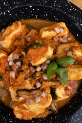 Pasta. Top view of traditional stuffed agnolottis with a tomato sauce with mushrooms, bacon and basil in a black dish on the wooden table.