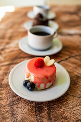 Colorful small fruity cupcakes on small white plates and cups of black coffee on wooden structure background