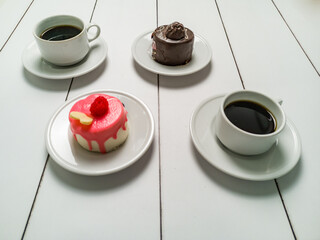 Colorful small fruity cupcakes on small white plates and cups of black coffee on light white background