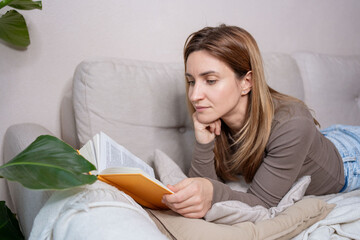  Woman relaxing on sofa and reading novel book at home.