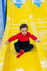 Happy, smiling little boy, the child goes down, slides down the plastic slide on the indoor...