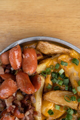 French fries. Top view of fried potatoes with sliced green onion, smoked sausages, crispy bacon and cheddar cheese sauce, in a metal dish on the wooden table.