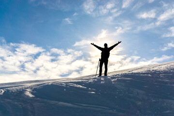 Silhouette of celebrating happy hiker man with raised arms on snowy winter mountain. Sun behind Person. - 574794121