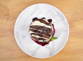 Sweet desserts. Top view of an ice cream cookie cake with berries compote in a white dish with a wooden background.