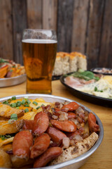 Eating at the restaurant. Closeup view of french fries with cheddar cheese, green onion and smoked sausages. Other dishes and a pint of beer in the background. 