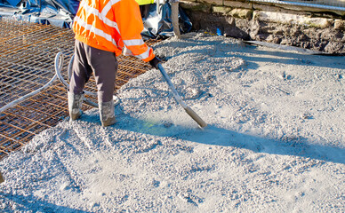 Builders pouring concrete slab with help of a concrete pump and using vibrating poker to compact...