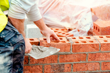 Close up of industrial bricklayer laying bricks on cement mix on construction site - obrazy, fototapety, plakaty