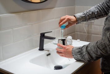 Effortless Oral Health: man Filling Water Flosser Tank with Mouthwash at Bathroom Basin