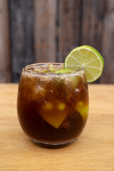 Cocktails. Closeup view of an alcoholic drink with Jägerinha, cola, ice and lime, with a wooden background. 