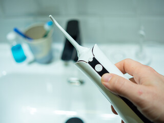 young man hand holding a domestic dental water flosser in front of a bathroom wash basin
