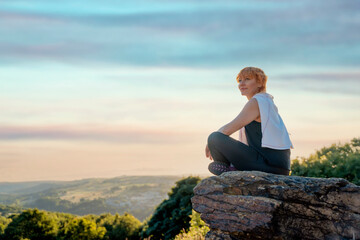 Naklejka na ściany i meble happy haired woman in sports suit sitting on a cliff after exercises