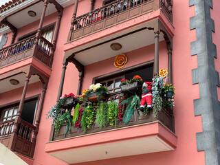 Balkon an roter Hausfassade mit Holzgeländer. Mit Pflanzen, Blumen und Weihnachtsmann ist die Brüstung geschmückt.