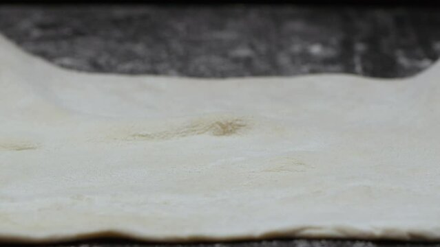 puff thin dough is placed on a dark table with flour and smoothed with hands. Slow motion