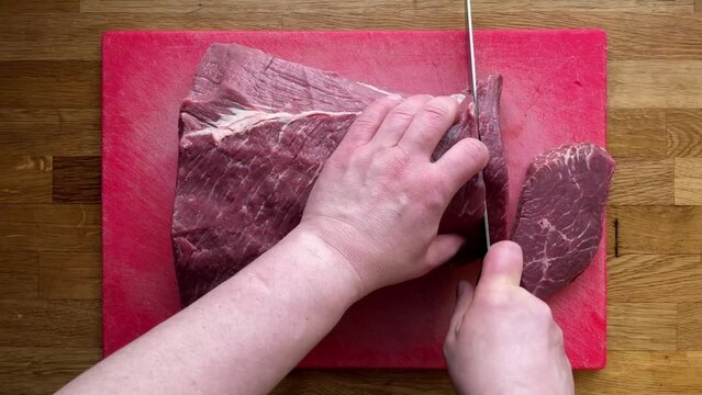 Men's Hands are cutting Beef silverside on the Read Cut Board, preparing Meat. The top view slicing a mature Herefordshire Beef Meat on the Wooden Kitchen Table.