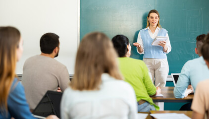 Young woman teacher is giving a lecture to students, standing near the blackboard in the university auditorium © JackF