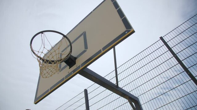 Shield with hoop and mesh on basketball ground under sky with light clouds low angle shot. Playground in city park
