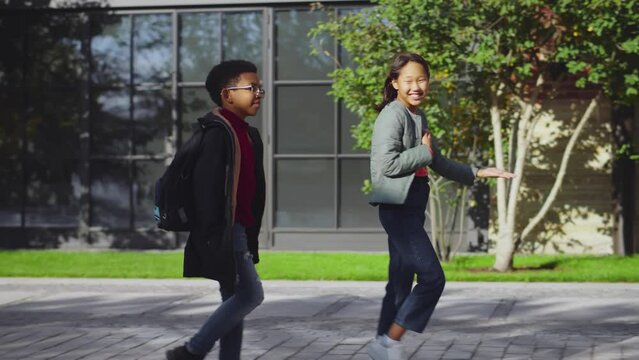 Cheerful asian and African American students talking while walking through campus park. Realtime