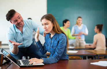 Annoying man student trying to talk with woman in classroom during recess.
