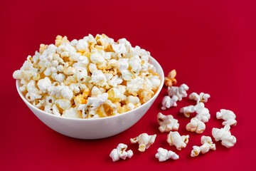 Scattered tasty cheese popcorn in white bowl isolated on red background. Flat lay, top view. Fast food, movie, cinema concept