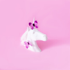 A white unicorn with purple butterflies on the horn and on the neck against pink background. Minimal surreal concept for spring summer season banner or wallpaper.