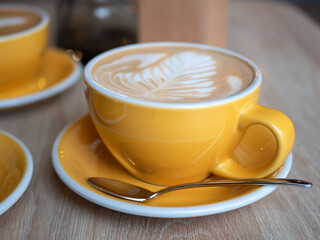 Yellow cup of cappuccino or latte on the table in the cafe. Ceramic cup of hot coffee, selective focus