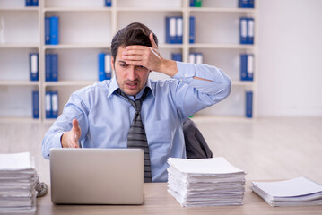 Fototapeta premium Young male employee and too much work at workplace