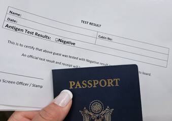 A negative test result document paper for traveling on a cruise ship alongside a woman's hand holding a passport.