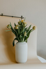 Bouquet of yellow tulips in modern vase during the process of photoshooting with light photo background, Still life 