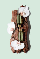 Two green glass cosmetic bottles on textured tree bark podium with white orchid flowers on pastel...