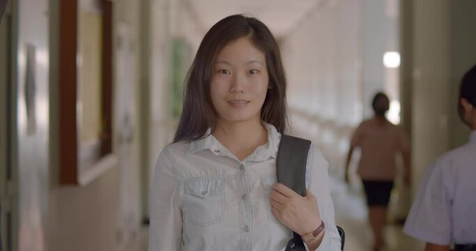 (Slow motion)A happy smiling Asian woman who is a Chinese teacher and teaches Chinese language in a secondary school of Thailand, standing with her laptop backpack.