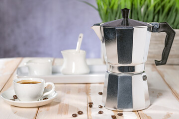 Italian geyser coffee maker and ceramic coffee cup on white table in the room.
