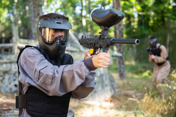 Fototapeta premium Excited paintball player in protective uniform aiming and shooting with guns