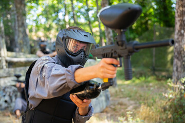 Excited paintball player in protective uniform aiming and shooting with guns