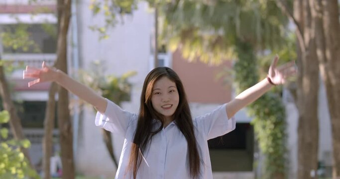 (Slow motion) A smiling Asian woman who is a Chinese teacher and teaches Chinese language in a secondary school of Thailand, walking in the school park and raises her hands happily in the evening.